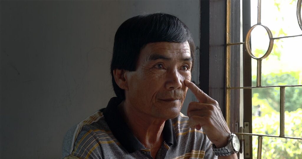 Câm, ein vietnamesischer Mann mittleren Alters, sitzt vor einem Fenster und deutet auf sein linkes Auge, während er seine Erinnerungen teilt.