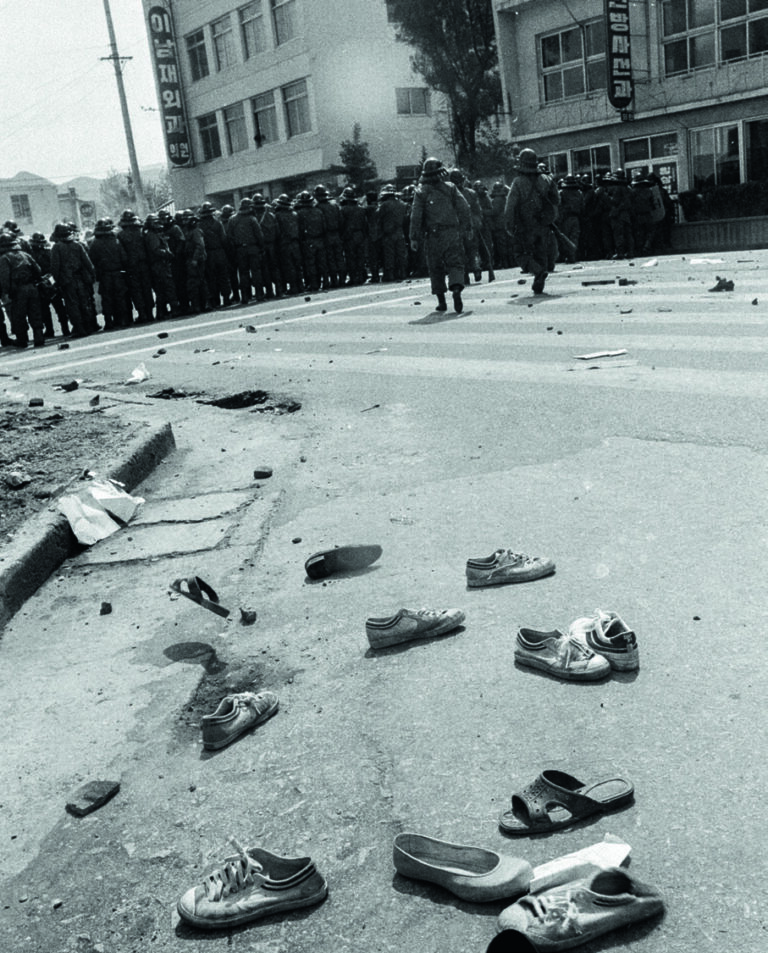Verstreute Turnschuhe auf der Straße im Vordergrund, eine Formation von Polizisten in voller Anti-Demonstrationsmontur im Hintergrund