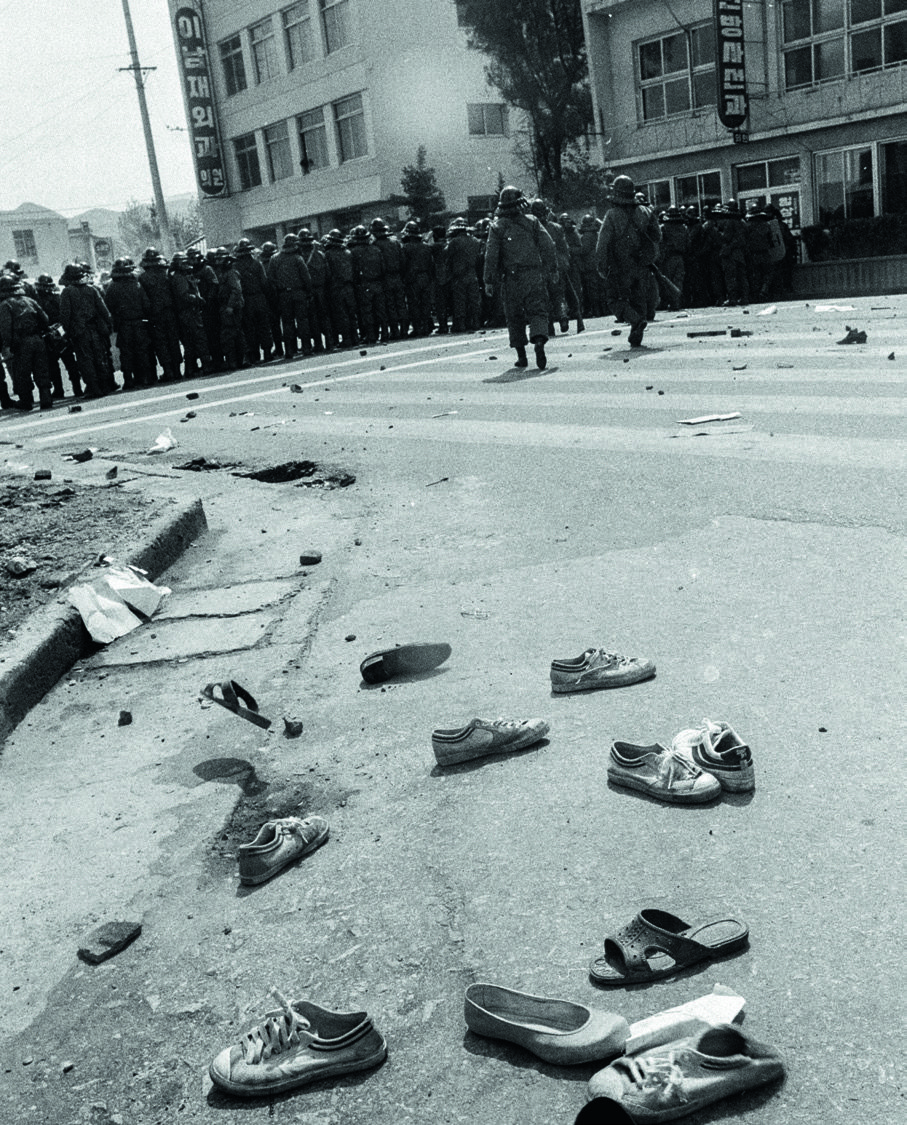 Verstreute Turnschuhe auf der Straße im Vordergrund, eine Formation von Polizisten in voller Anti-Demonstrationsmontur im Hintergrund