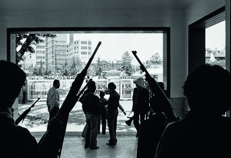 Mitglieder der Bürgerarmee stehen mit gezückten Gewehren in einem Raum ohne Schaufensterscheiben.