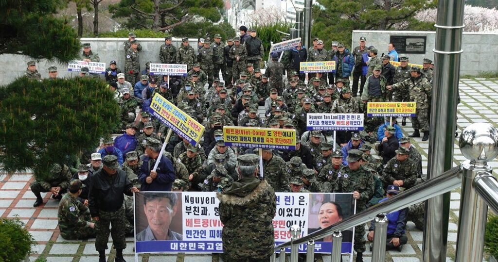 Eine Gruppe von uniformierten koreanischen Kriegsveteranen protestiert überwiegend sitzend mit Plakaten in der Hand